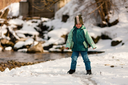 河边散步摄影照片_冬天在河边散步的小男孩；这个孩子站在冰上