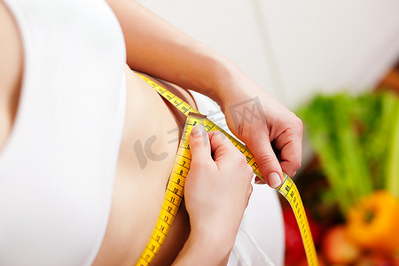 瘦和美丽的女人（只有躯干）测量她的腰用卷尺，在背景水果在一个碗