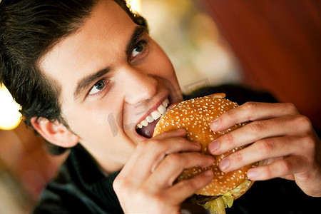 在餐馆或餐馆里吃汉堡包的人，他饿了，用可用光线拍摄，非常有选择性地吃了一口