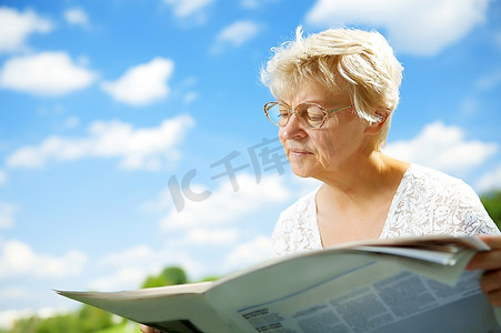 老报纸摄影照片_在天空的衬托下拿着报纸的老妇人