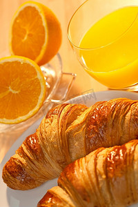 健康的欧式早餐，牛角面包糕点，橙汁，橙子在金色清晨的阳光下照亮。