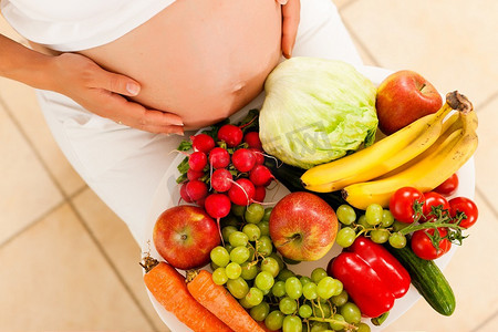 怀孕与营养--孕妇腿上放着一碗水果和蔬菜