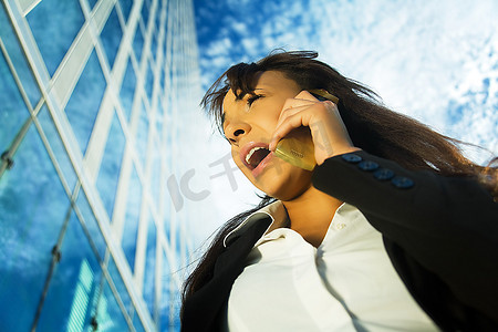 一名穿着商务服装的黑发女子在一座现代商业大楼前使用手机