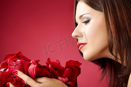 侧面的女孩闻玫瑰花瓣，孤立在一个红色背景