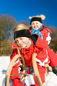两个小孩子和他们的雪橇在山顶上的雪等待开始的乐趣