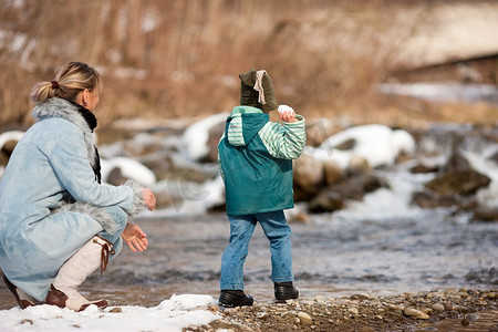 一家人--母亲和儿子--冬天沿着河岸散步；孩子在扔雪球