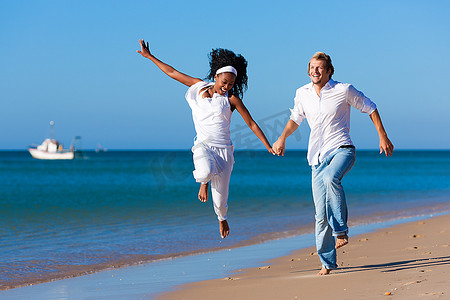 黑人妇女摄影照片_夫妇-黑人妇女和白人男子-步行和跑步下来的海滩在他们的假期