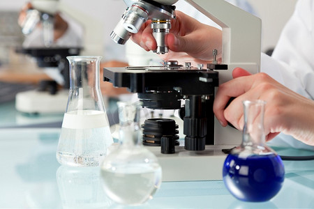 医疗实验室摄影照片_在有烧瓶和医疗设备的实验室环境中使用显微镜的医学或科学研究人员。
