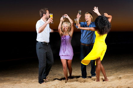海滩上的人们(两对情侣)在夕阳下开着派对，玩得很开心，他们穿着时髦的休闲服，跳舞