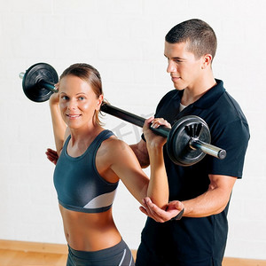 一名女子和她的私人健身教练在健身房用杠铃练习力量体操