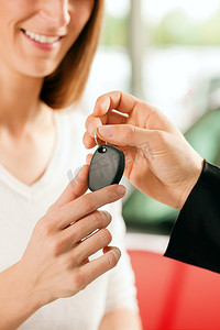 经销商摄影照片_一名女子在汽车经销商购买一辆汽车，销售代表给了她钥匙，微距镜头聚焦在手和钥匙上