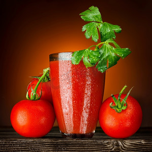 木桌上放着一杯湿的番茄汁，上面装饰着欧芹和成熟的番茄串。