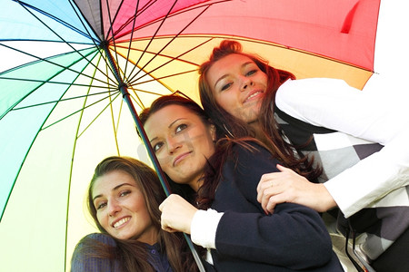 快乐微笑的女朋友们留在五颜六色的伞下