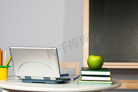 课桌上放着苹果、电脑和课本，背对着黑板。专注于计算机