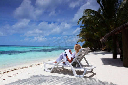 一位拿着白纸的女商人躺在热带海岸的躺椅上