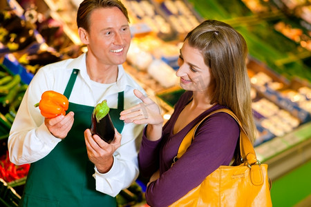 一名妇女在超市的菜架上买杂货，一名店员正在帮助她