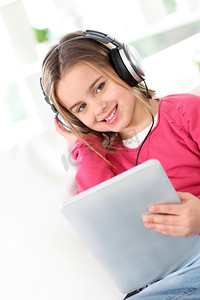 儿童歌曲大赛摄影照片_戴着耳机和电子平板电脑的小女孩