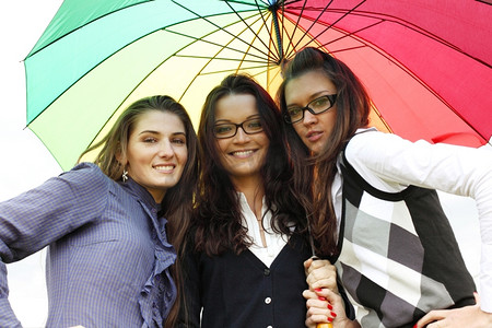 女朋友们摄影照片_快乐微笑的女朋友们留在五颜六色的伞下