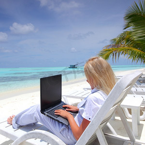 一位拿着笔记本电脑的女商人躺在热带海岸的躺椅上