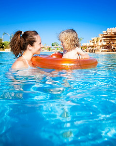 在热带度假胜地海边的游泳池里，快乐的孩子和妈妈在蓝色的水里玩耍。暑假概念