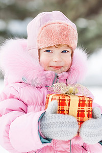 冬天小朋友摄影照片_冬天公园里拿着圣诞礼物的快乐小朋友。户外拍摄