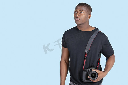 一名年轻的非洲裔美国男子，手持数码相机，抬头看着蓝色背景