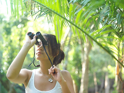 长筒望远镜摄影照片_热带雨林中的年轻女子通过双筒望远镜看