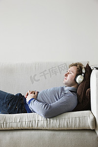戴耳机的人躺在沙发在客厅，侧视图