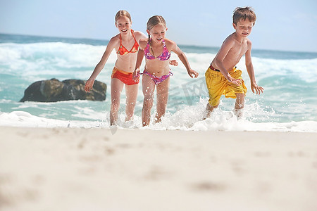 三个孩子(5-6 7-9 10-12)在海滩上跑步