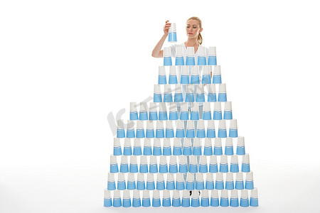 开业大吉金字摄影照片_一名女子在白色背景下将塑料杯堆成金字塔状