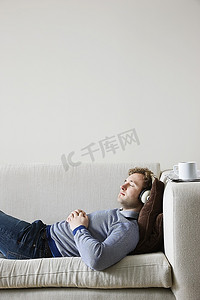 戴着耳机的男子躺在客厅的沙发上，侧视
