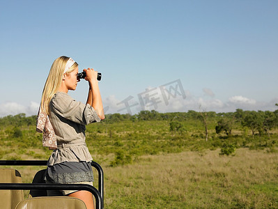 在狩猎中的年轻女子站在吉普车里透过双筒望远镜侧视