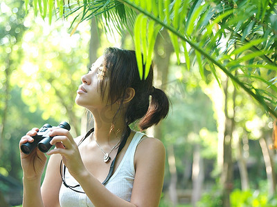 热带森林里的年轻女子手持双筒望远镜