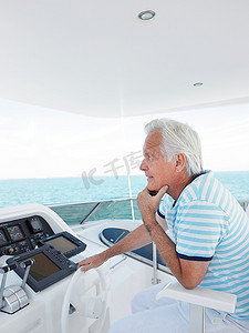 一名中年男子坐在游艇侧景旁掌舵
