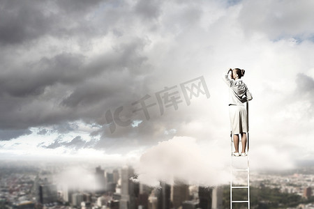 眺望远方人摄影照片_女商人站在梯子上，在城市的背景下眺望远方