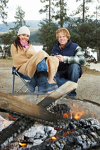 穿着保暖衣服的年轻夫妇坐在篝火旁