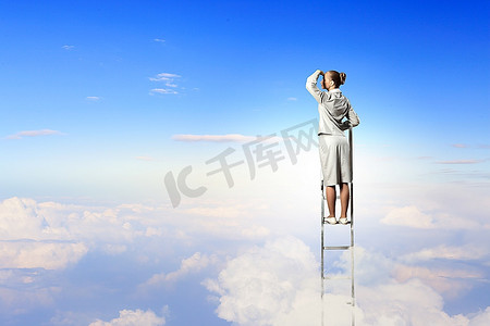 站在梯子上的女商人在多云的背景下眺望远方