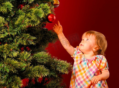 伸手搭车摄影照片_婴儿在树旁伸手去拿圣诞玩具