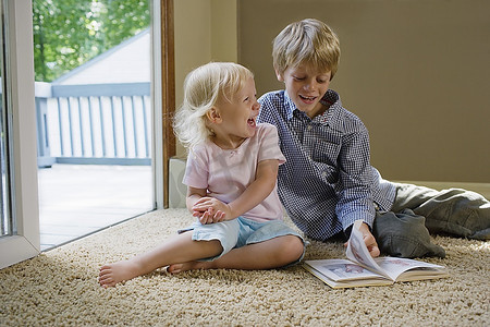 5.12汶川摄影照片_小男孩(5-6)和姐姐(1-2)抱着书坐在地毯上，笑着