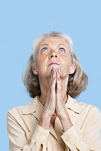 一位老年妇女在蓝色背景下双手合十祈祷