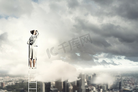 女商人站在梯子上，在城市的背景下眺望远方