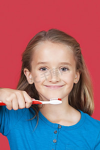 肖像的女孩举行牙刷反对红色背景
