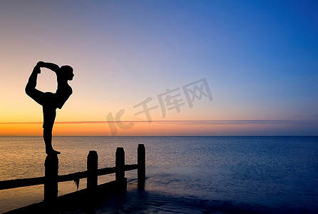 日落时分，年轻女子在空荡荡的海滩上锻炼的剪影