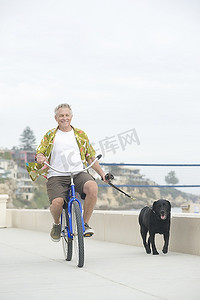 一位老年男子骑自行车练狗