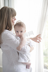 母亲抱着一个男婴站在窗前看