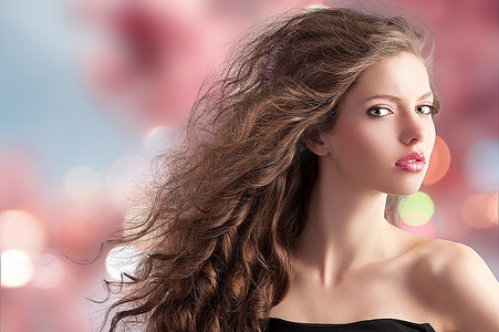 美丽时尚肖像--一位年轻可爱的黑发女子，留着长长的卷发，樱花背景下的发型在风中飘扬