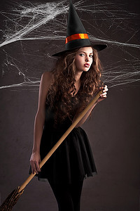 可爱的年轻模特打扮成万圣节女巫，戴着一顶巨大的橙色黑色帽子