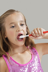 年轻女孩刷牙反对灰色背景