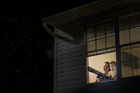 十几岁的男孩拿着望远镜站在敞开的窗户前看夜空