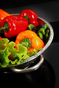 蔬菜落摄影照片_新鲜洗净的新鲜蔬菜在隔绝在黑色背景上的金属滤器中。